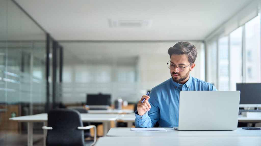 Jeune homme d'affaires latin occupé travaillant au bureau à l'aide d'un ordinateur portable vérifiant des documents. Homme d'affaires professionnel sérieux, responsable des ressources humaines analysant le rapport comptable et faisant un aperçu du projet. Partage de la valeur ajoutée